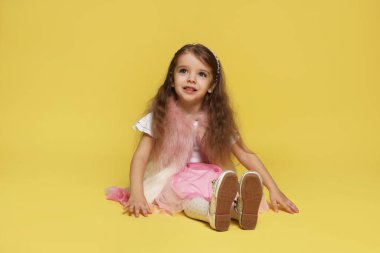 Sarı arka planda kürklü ve etekli mutlu küçük kız.