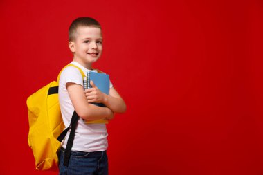 Sırt çantası ve kırmızı arka planda defterleri olan sevimli küçük çocuk, mesaj için yer var.