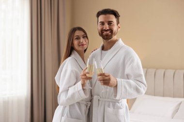 İçeride köpüklü şarap bardakları olan bornozlu mutlu çift.