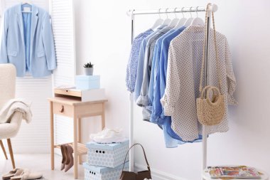 Beyaz duvarın yanında askıda asılı farklı şık kıyafetler, çantalar ve ayakkabılar.