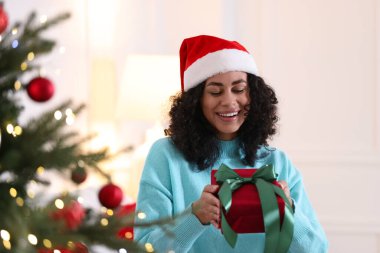 Noel Baba şapkalı ve hediyeli mutlu kadın Noel ağacının yanında.