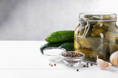 Kavanozda salatalık turşusu ve beyaz ahşap masada malzemeler, yakın plan. Metin için boşluk