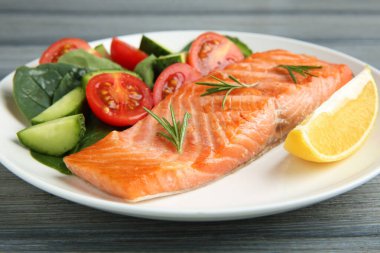 Izgara somon, limon, biberiye ve salata. Gri ahşap masada. Yakın plan.