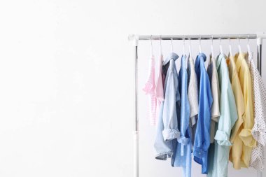 Beyaz duvarın yanında askıda asılı farklı şık kıyafetler, metin için boşluk.