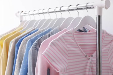 Beyaz duvarın yanında askıda asılı farklı şık kıyafetler, yakın plan.