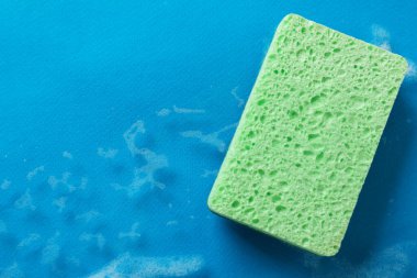 Açık mavi arka planda mutfak süngeri ve köpük, üst manzara. Metin için boşluk