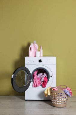 Modern çamaşır makinesi, deterjan ve zeytin duvarının yanındaki kıyafetler.