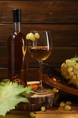 Lezzetli beyaz şarap, cam, şişe, üzüm ve yapraklar ahşap masada.