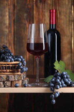 Bardakta kırmızı şarap, şişe ve üzümler ahşap masada, yakın plan.