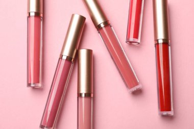 Pembe arka planda farklı dudak parlatıcıları, düz yatış