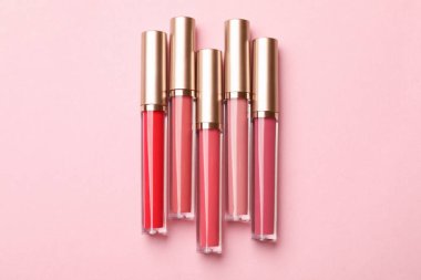 Pembe arka planda farklı dudak parlatıcıları, düz yatış