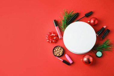 Kırmızı arka planda makyaj ürünleri ve Noel dekoru olan düz bir kompozisyon. Metin için boşluk