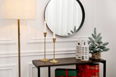 Ayna, yanan mumlar ve Noel dekoru beyaz duvarın yanındaki konsol masasında.