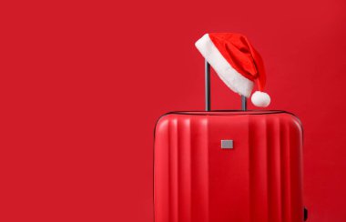 Noel tatili. Kırmızı arka planda Noel Baba şapkası olan bavul, metin için boşluk
