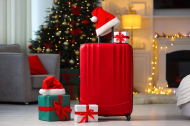 Christmas vacation. Suitcase with Santa hat and gift boxes indoors