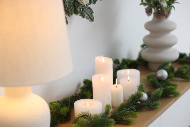 Beyaz duvarın yanındaki dolapta Noel süsleri ve yanan mumlar, yakın plan. İç tasarım
