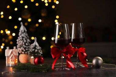 Kırmızı şarap kadehleri ve ahşap masanın üzerinde bulanık ışıklarla çevrili Noel süslemeleri.