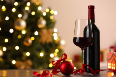 Bir kadeh kırmızı şarap, şişe ve Noel süsü ahşap masada arka planda bulanık ışıklar, mesaj için yer