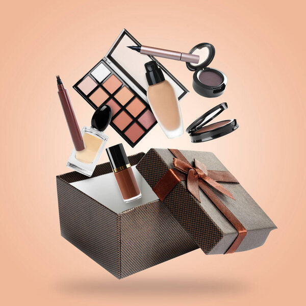 Makeup products falling into gift box on beige background. Decorative cosmetics