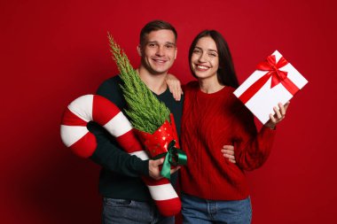 Mutlu çift Noel hediyesiyle, thuja ağacı ve kırmızı arka planda dekoratif şeker kamışı.