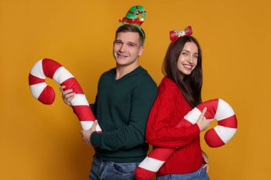 Sarı arka planda dekoratif şeker kamışları olan Noel bantlı mutlu çift