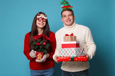 Noel aksesuarları, saksısı ve açık mavi arka planda hediyeleri olan mutlu çift.