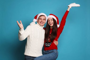 Noel Baba şapkalı gülümseyen çift açık mavi arka planda eğleniyor. Mutlu Noeller ve mutlu yıllar.