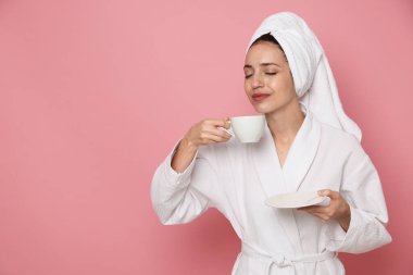 Pembe arka planda bir fincan kahveyle bornozlu bir kadın. Metin için boşluk