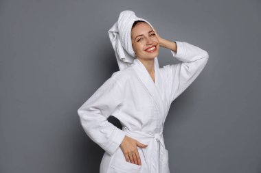 Gri arka planda havluya sarılı saçı olan bornoz giyen güzel bir kadın.