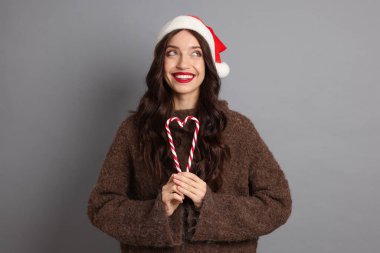 Gri arka planda Noel Baba şapkası ve şeker kamışı olan güzel bir kadın. Noel sezonu
