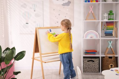 Küçük kız alfabeyi içeride harflerle beyaz tahtanın yanında öğreniyor.