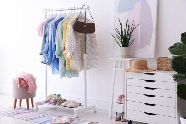 Beyaz duvarın yanında askıda asılı farklı şık kıyafetler, çanta ve ayakkabılar.