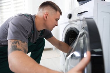 Tamirci evde bozuk çamaşır makinesini inceliyor.