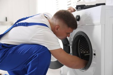 Üniformalı tamirci evde bozuk çamaşır makinesini tamir ediyor.