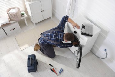 Tamirci evde bozuk çamaşır makinesini tamir ediyor.