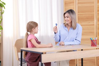 Konuşma terapisti kız alfabeyi öğretiyor. İçerideki ahşap masada harflerle.