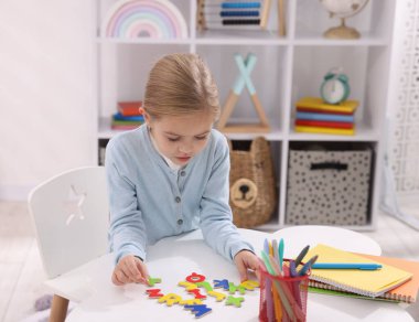 Beyaz masada harflerle alfabe öğrenen küçük bir kız.
