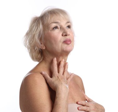 Yaşlı kadın beyaz arka planda boynuna dokunuyor.