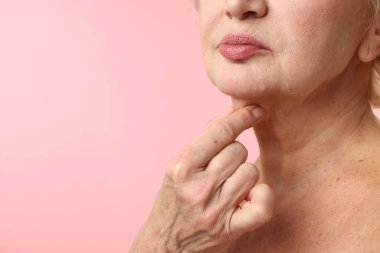 Üst düzey kadın açık pembe arka planda boynuna dokunuyor, yakın plan. Metin için boşluk