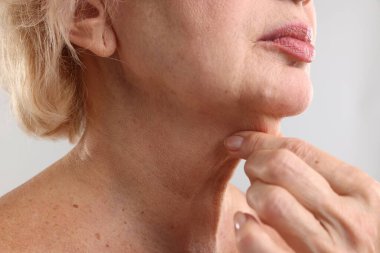 Üst düzey kadın açık gri arka planda boynuna dokunuyor, yakın plan.