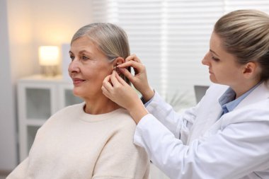 Doktor klinikte hastanın kulağına işitme cihazı takıyor.
