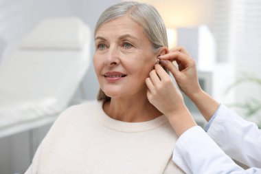 Doktor klinikte hastanın kulağına işitme cihazı takıyor.