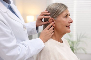 Doktor klinikte hastanın kulağına işitme cihazı takıyor.