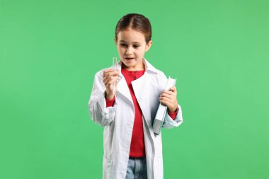 Yeşil arka planda kitap ve test tüpüyle laboratuvar önlüklü küçük kız şaşırdı. Çocuk ve bilim