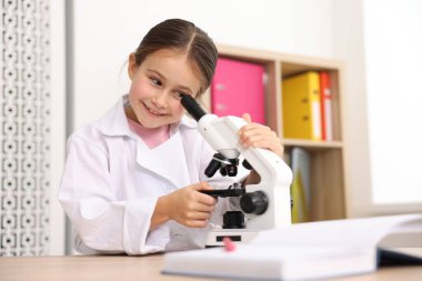 Masada mikroskopla gülümseyen küçük bir kız. Çocuk ve bilim