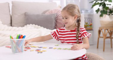 Beyaz masada harflerle alfabe öğrenen küçük bir kız.