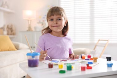 Beyaz masa içinde fırça çizen küçük kız.