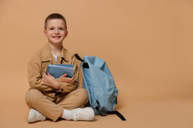 Bej arka planda not defteri ve sırt çantası olan şirin bir çocuk. Mesaj için yer var.