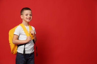 Kırmızı arka planda sırt çantası olan sevimli küçük çocuk, mesaj için yer var.