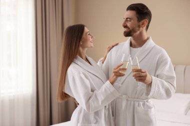 İçeride köpüklü şarap bardakları olan bornozlu mutlu çift.